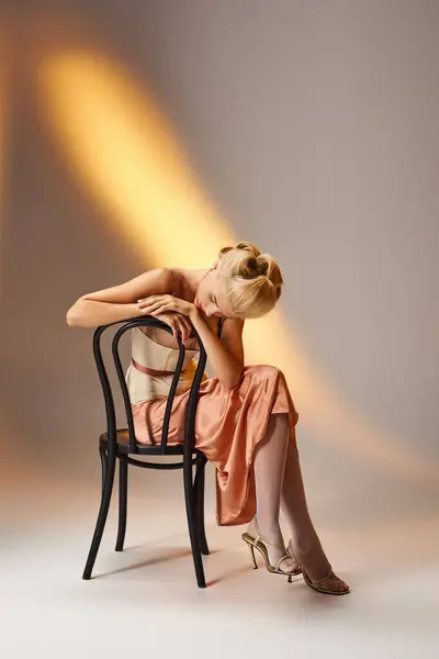 Гламурная молодая девушка в стильном наряде позирует на черном стуле на сером фоне — стоковое фото