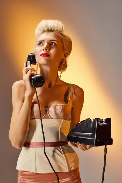 Disgruntled blonde girl with red lips talking on retro phone against gray background — Stock Photo