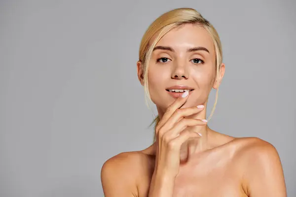 Charmante blonde Mädchen in ihren 20ern berühren ihre Lippen mit der Hand vor grauem Hintergrund — Stockfoto