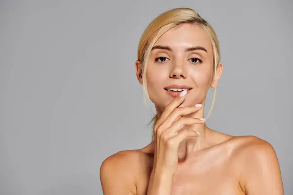 Charming blonde girl in her 20s touching her lips with hand against gray background — Stock Photo