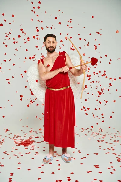 Homme barbu habillé en Cupidon tir à l'arc sous les confettis en forme de coeur, st Saint-Valentin fête — Photo de stock