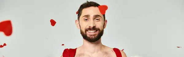Drôle homme Cupidon souriant à la caméra sous rouge confettis en forme de coeur, st Saint-Valentin fête, bannière — Photo de stock