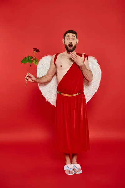 Pleine longueur de l'homme étonné en costume de Cupidon avec rose et bouche ouverte sur le rouge, Saint Valentin — Photo de stock