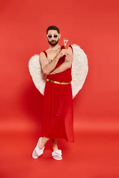 Cool bearded man in cupid costume posing with champagne glass on red, Saint Valentines party — Stock Photo