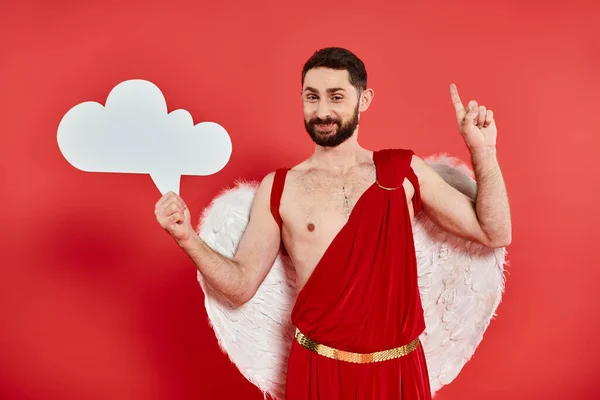 Hombre barbudo alegre en traje de Cupido con burbuja de pensamiento vacío blanco mostrando signo de idea en rojo - foto de stock