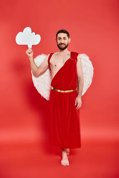 Full length of barefoot bearded man dressed as cupid with white empty thought bubble on red — Stock Photo