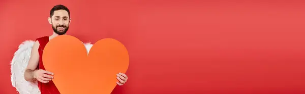 Romantic bearded man in cupid costume with huge paper heart on red, Saint Valentines day, banner — Stock Photo