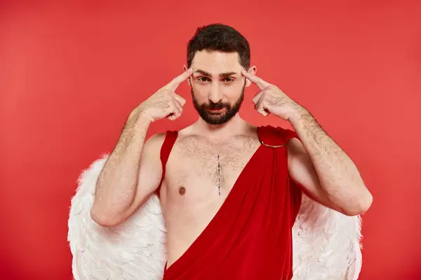 Homme barbu réfléchi en costume de Cupidon toucher la tête en regardant la caméra sur rouge, st Saint-Valentin — Photo de stock