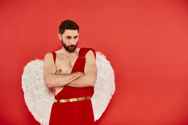 Serious and thoughtful cupid man with folded arms standing on red backdrop, Saint Valentines concept — Stock Photo