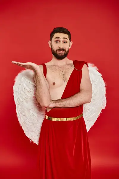 Discouraged bearded cupid pointing with hand and looking at camera on red, Saint Valentines day — Stock Photo