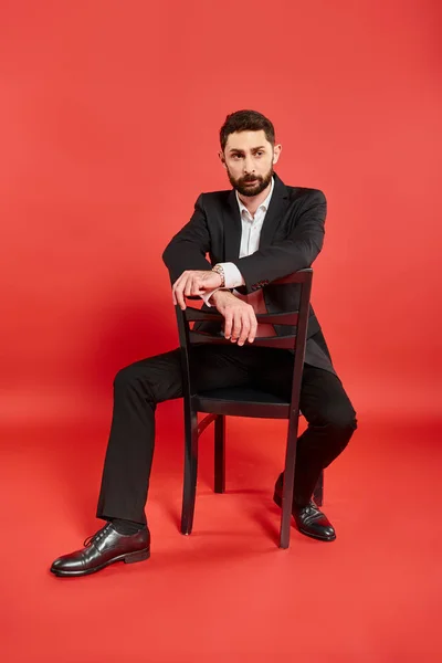 Повна довжина елегантного заможного бізнесмена в чорному костюмі, сидячи на стільці і дивлячись на червоний — стокове фото