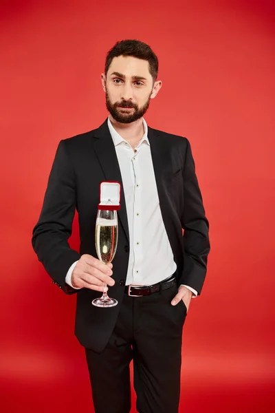 Man in black suit with champagne glass and gift box with jewelry ring on red, st valentines day — Stock Photo