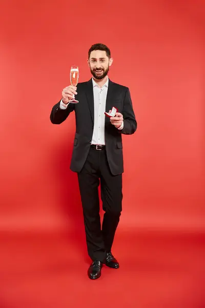 Homem elegante feliz em terno preto com copo de champanhe e caixa de jóias no dia dos namorados vermelho, st — Fotografia de Stock