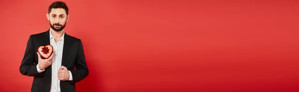 Sorrindo homem elegante em terno preto com coração em forma de dia dos namorados presente no vermelho, banner — Fotografia de Stock