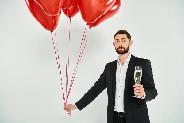 Elegant man with red heart-shaped balloons and champagne glass on grey, st valentines concept — Stock Photo