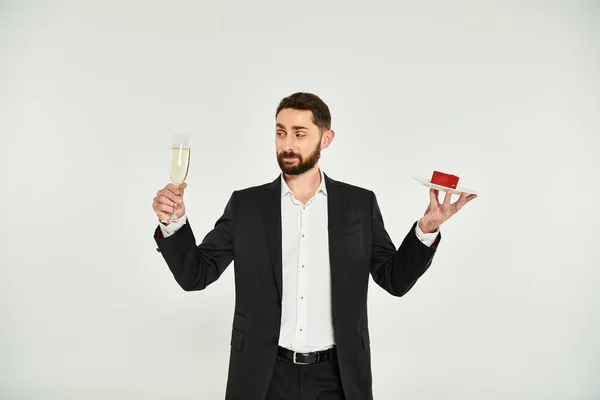 Stilvoller Mann im schwarzen Anzug mit Champagnerglas und herzförmiger Torte auf grau, Valentinstag — Stockfoto