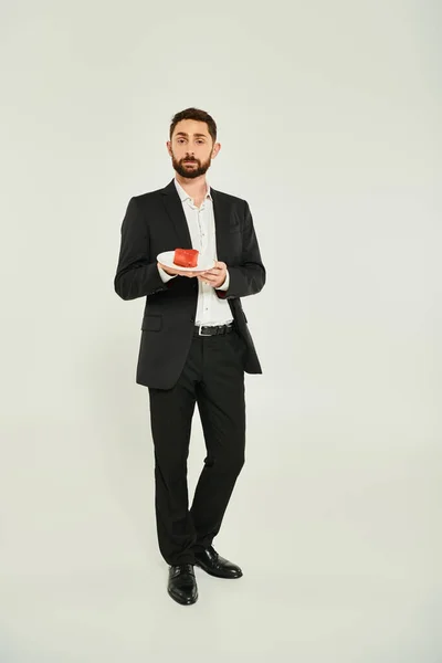 Full length of sharp-dressed man holding plate with heart-shaped cake on grey, st valentines concept — Stock Photo