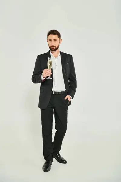 Handsome businessman in black suit with champagne and hand in pocket on grey, st valentines concept — Stock Photo