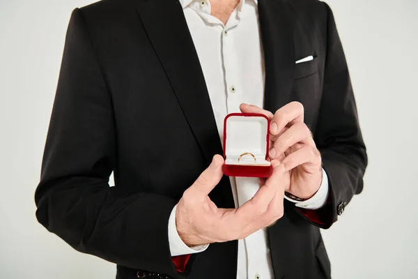 Vue recadrée de l'homme en costume noir montrant boîte à bijoux avec bague sur gris, concept st valentines — Photo de stock