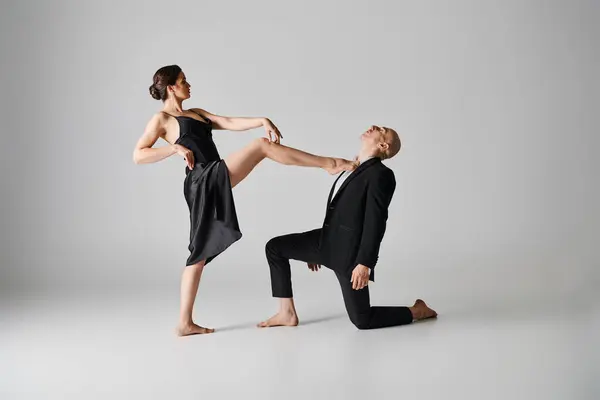 Joven mujer descalza en vestido negro realizando baile apasionado con el hombre sobre fondo gris - foto de stock