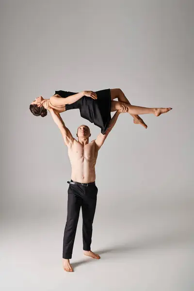 Shirtless man lifting young woman in black dress while performing dress on grey background — Stock Photo