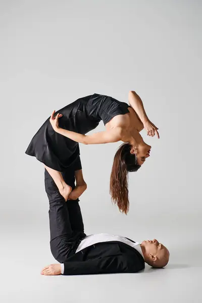 Гибкая женщина в черном, балансирующая на босых ногах своего партнера по танцам на сером фоне — стоковое фото
