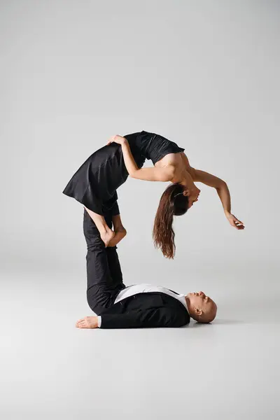 Flexible young woman in black dress balancing on bare feet of her dancing partner on grey backdrop — Stock Photo
