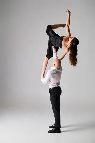 Сильний чоловік піднімає гнучку молоду жінку в чорній сукні під час виконання танцю на сірому фоні — стокове фото