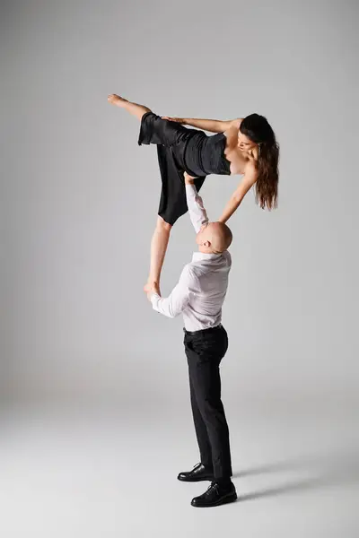 Starker Mann hebt brünette Frau in schwarzem Kleid, während er vor grauem Hintergrund tanzt — Stockfoto