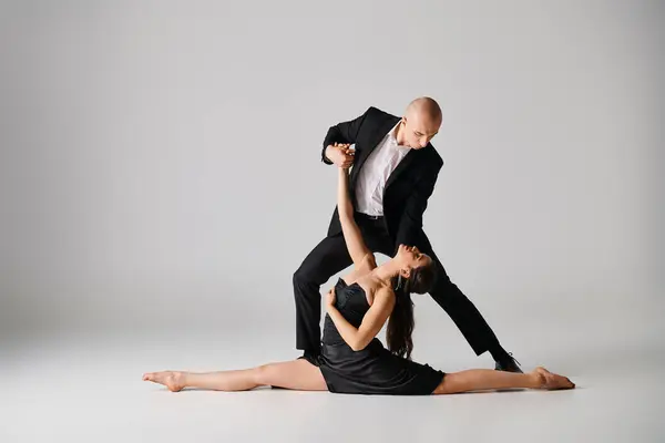 Homem de traje preto apoiando acrobata fêmea descalça em pose dividida durante a performance em estúdio — Fotografia de Stock