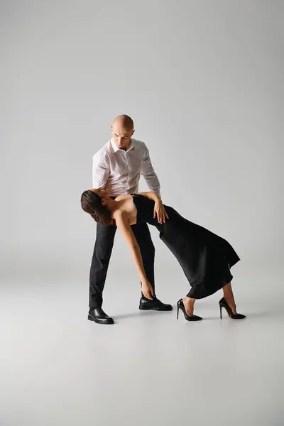 Чоловік в чорному вбранні, що підтримує жіночу танцівницю в одязі, виступаючи разом у сірій студії — стокове фото
