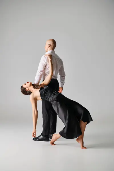 Homem de vestido preto apoiando dançarina no vestido enquanto se apresentam juntos em estúdio cinza — Fotografia de Stock
