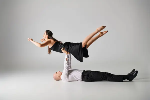Чоловік танцюрист лежить на підлозі і піднімає тіло жінки в одязі під час танцювального виступу на сірому — стокове фото