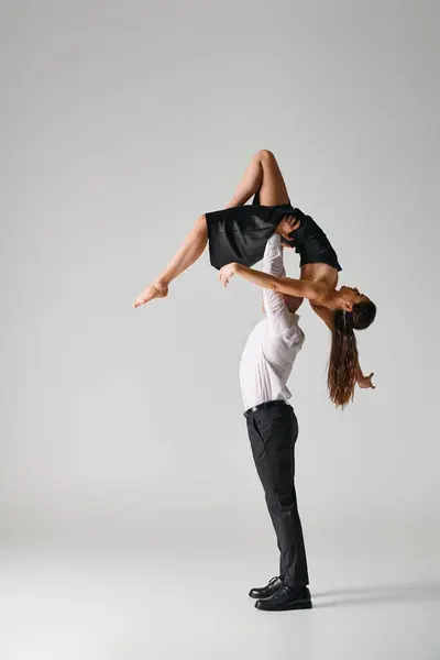 Man in suit lifting body of woman in black dress during dance performance on grey backdrop — Stock Photo