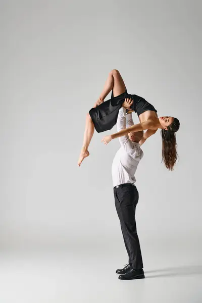 Dancer in suit lifting body of woman in black dress during performance on grey backdrop in studio — Stock Photo