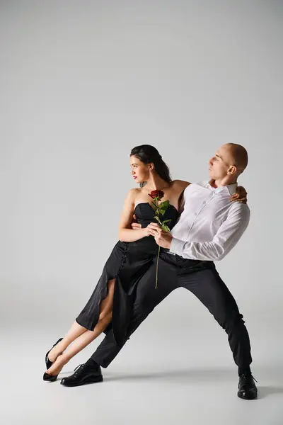 Elegant dance motion of young couple, woman holding red rose and man in formal attire in studio — Stock Photo