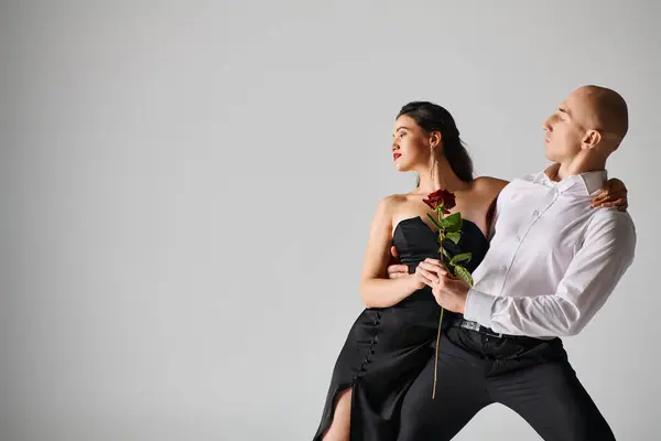 Dramatic dance motion of young couple, woman holding red rose and man in formal attire in studio — Stock Photo