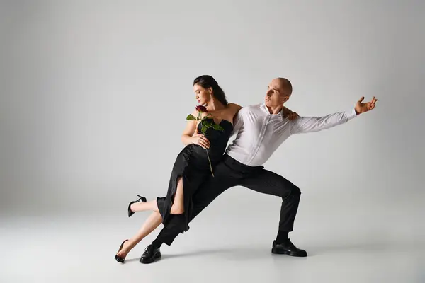 Dance motion of young couple, brunette woman holding red rose and man in formal attire in studio — Stock Photo