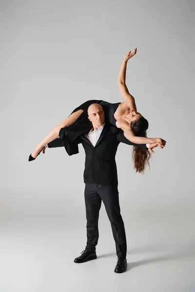 Starke männliche Tänzerin hebt brünette Frau in Kleid und High Heels im Studio auf grauem Hintergrund — Stockfoto