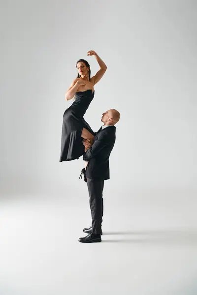 Homem levantando jovem mulher elegante em vestido preto e saltos altos equilibrando durante o desempenho — Fotografia de Stock