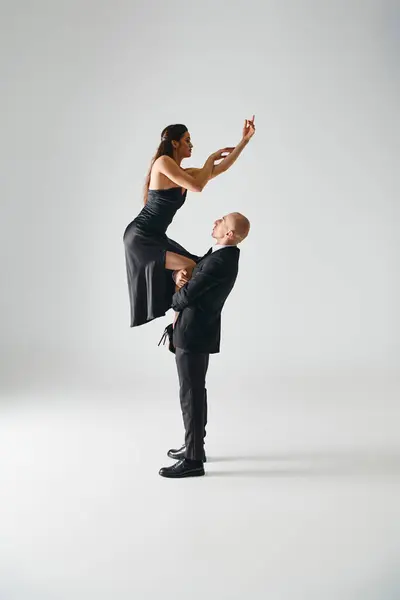 Man lifting young brunette female dancer in black dress and high heels balancing during performance — Stock Photo