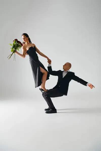 Homme soulevant jeune femme élégante en robe noire tenant des roses rouges et équilibrant pendant la performance — Photo de stock