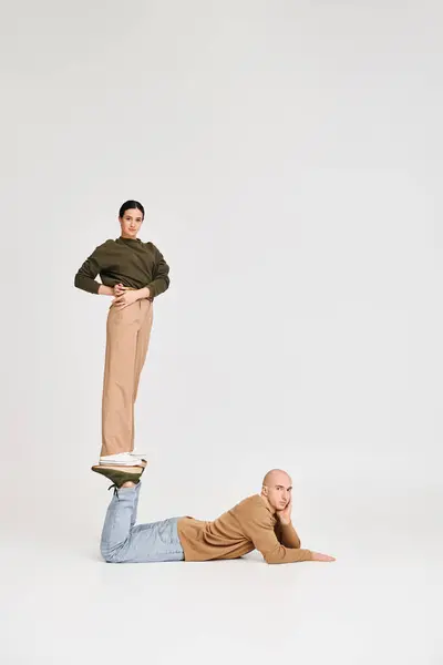 Young woman in casual attire balancing on legs of man in a playful pose in studio on grey backdrop — Stock Photo