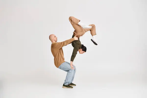 Paar in lässiger Kleidung beim akrobatischen Balanceakt im Studio vor grauem Hintergrund — Stockfoto