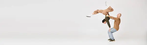 Casal em desgaste casual realizando um equilíbrio acrobático intrincado em estúdio em fundo cinza, banner — Fotografia de Stock