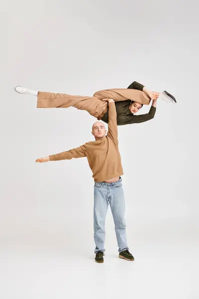 Paar in lässiger Kleidung führt dynamische akrobatische Balance im Studio auf grauem Hintergrund vor — Stockfoto