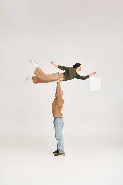 Homme fort en tenue décontractée soulevant femme avec sac à provisions, équilibrage dans une pose ludique en studio — Photo de stock