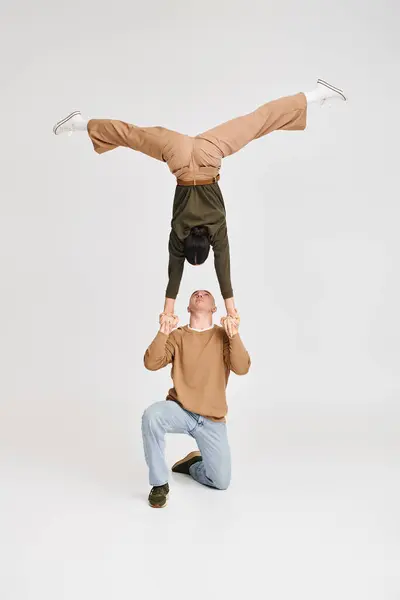 Giocoso duo acrobata con donna in testiera sorretta da uomo inginocchiato in studio su sfondo grigio — Foto stock
