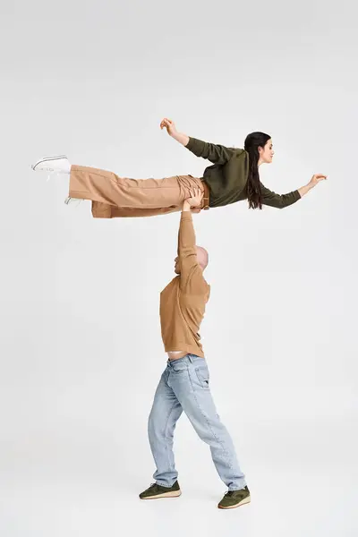 Художній акробатний дует з чоловіком, що піднімає і підтримує брюнетку в студії на сірому фоні — стокове фото