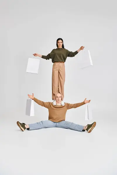 Coppia acrobatica con shopping bag, giovane donna in piedi sulle spalle dell'uomo su sfondo grigio — Foto stock